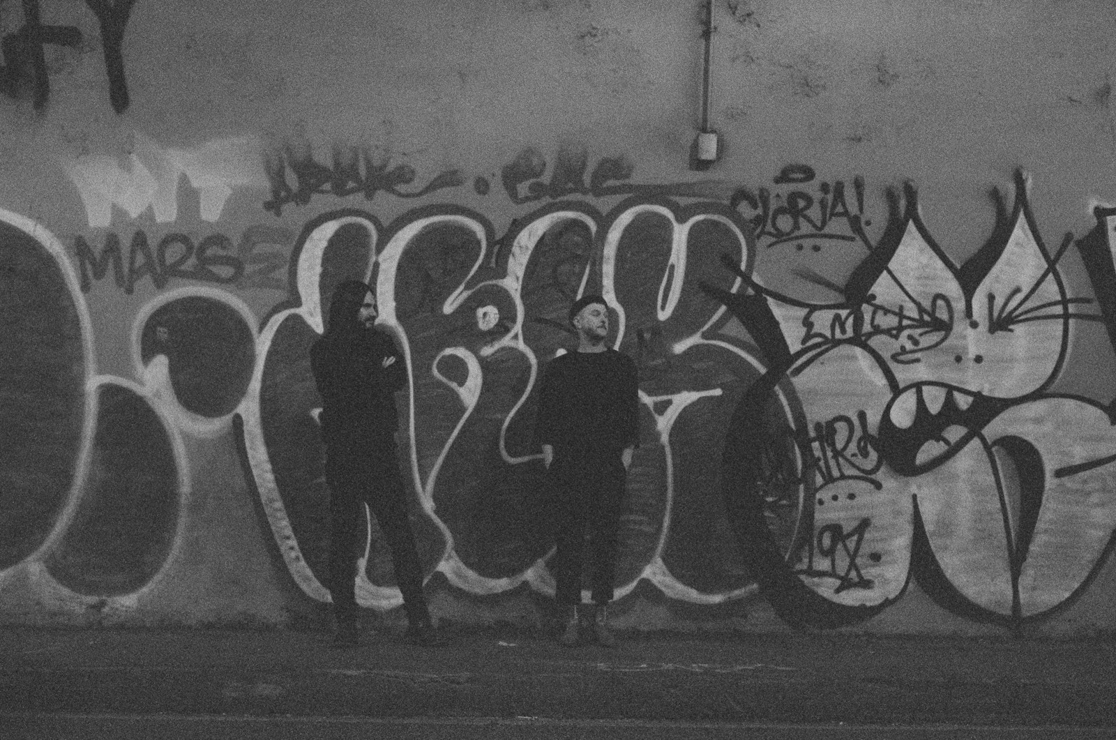 Two people stand in front of graffiti.